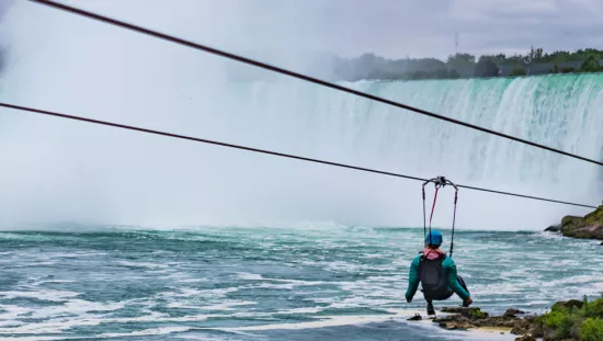A person rides a zipline in front of the Niagara Falls.